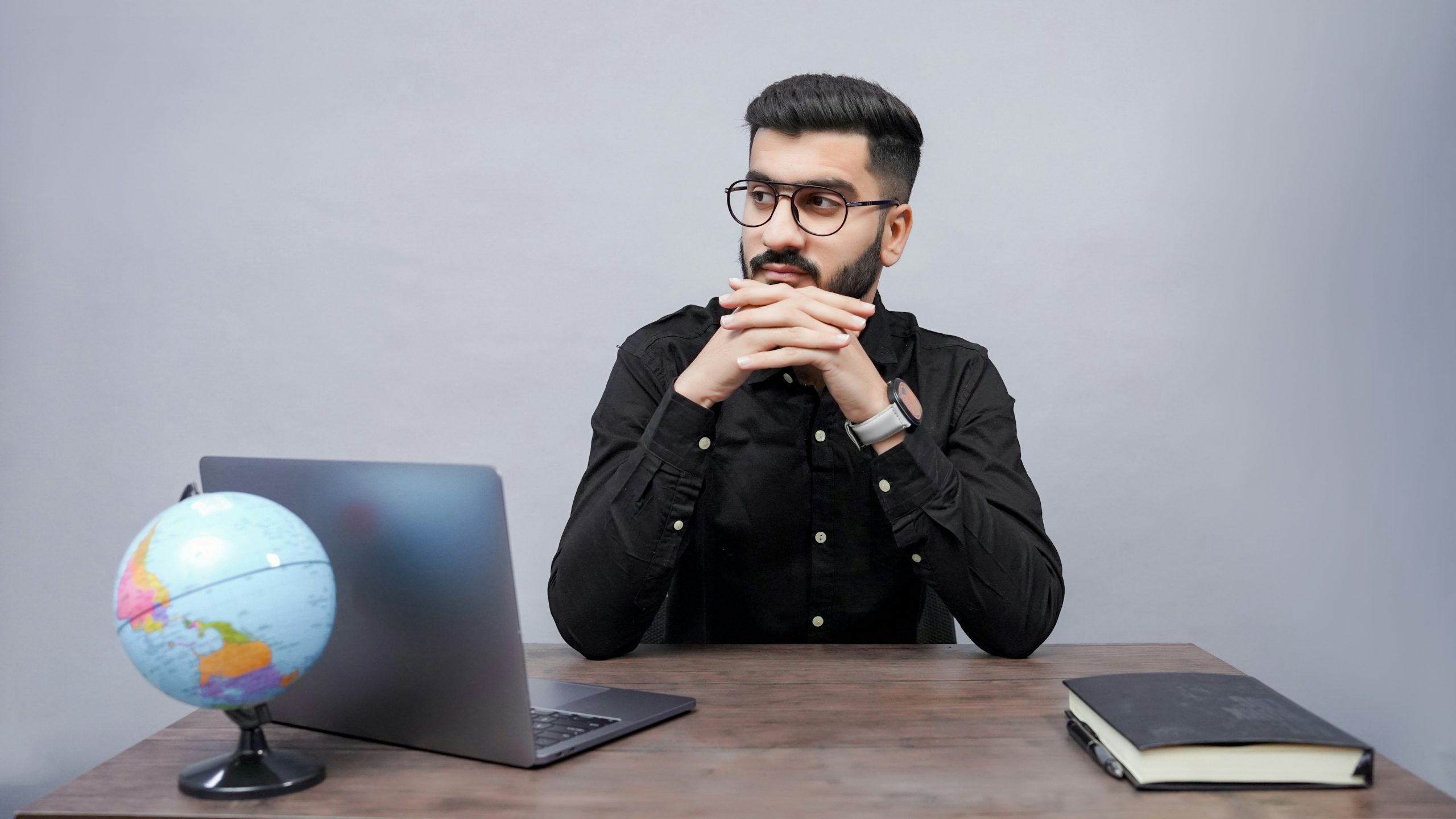 businessman deep in thought, sitting at a desk with a laptop, globe, and book